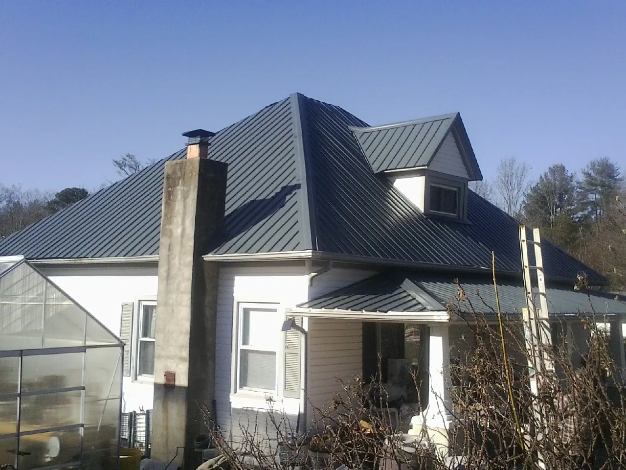 Dark blue standing seam metal roof on a white farmhouse with dormer — Slate & Tile Roof Repair by Roofing Brothers in Conshohocken