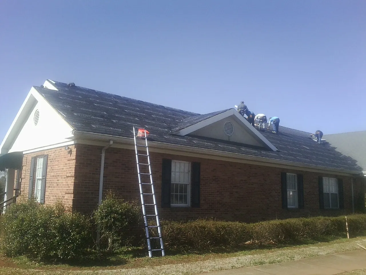 Crew tearing shingles off a brick ranch roof with a ladder set — Metal Roof Repair work by our crew in Conshohocken