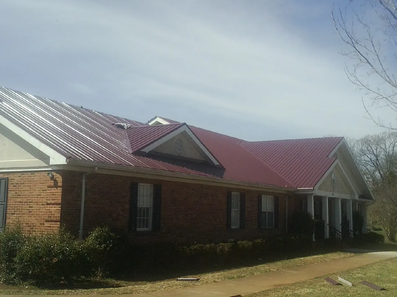 Red metal roof with gabled entries on a long brick building, from a Hail Damage Roof Repair job in Conshohocken