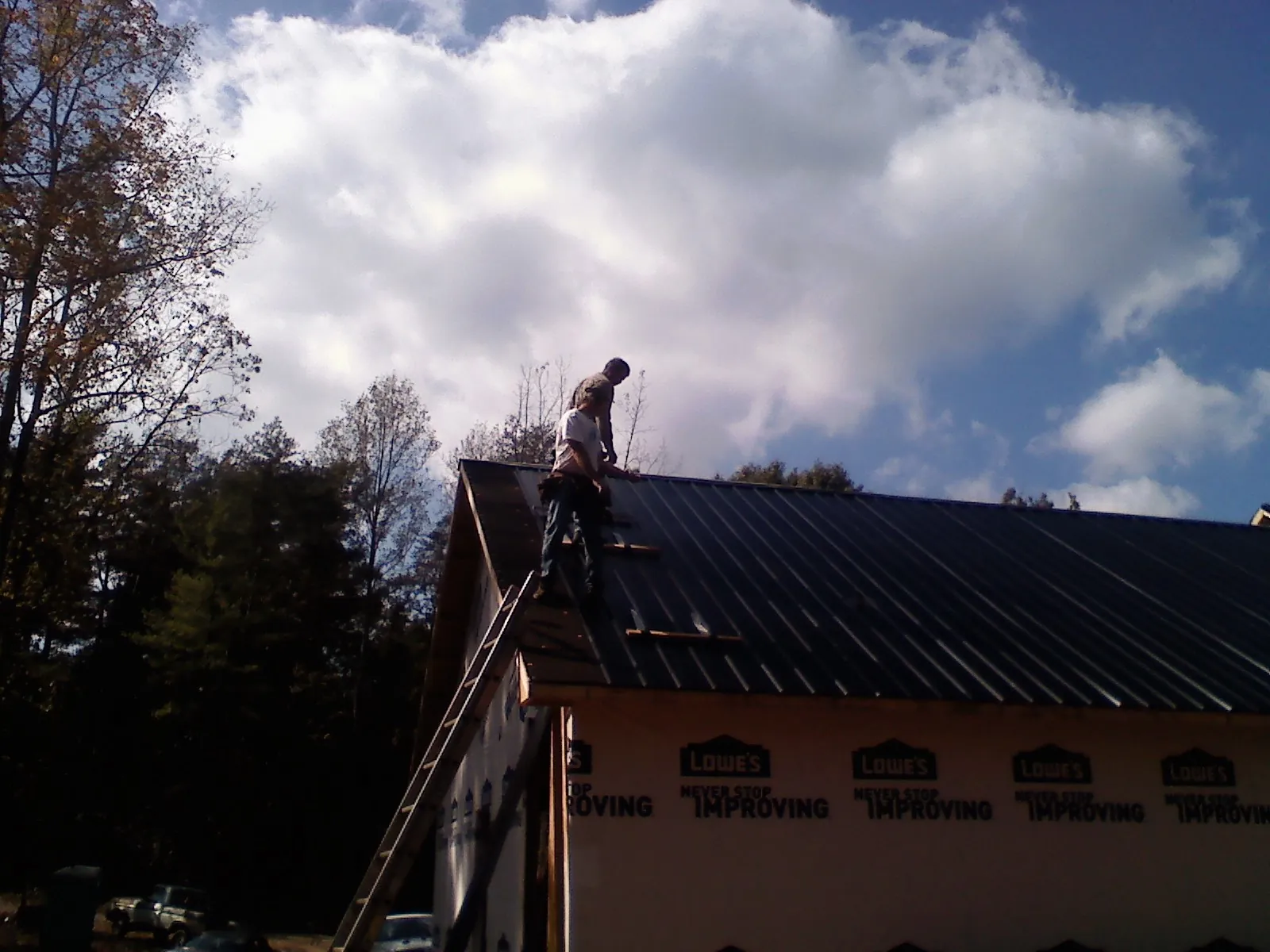 Roofer fastening dark metal panels high against a cloudy sky, from a Roof Inspection job in Conshohocken