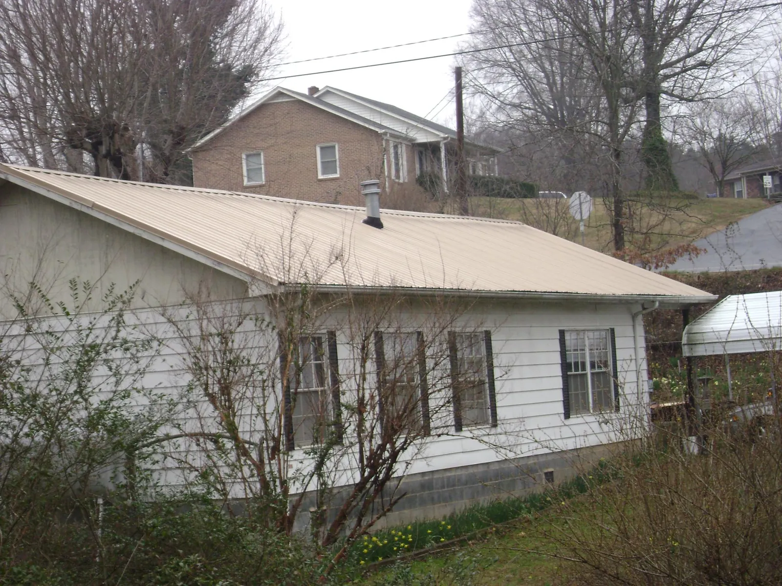 Tan metal roof on a white sided house set into a hillside — Commercial Roofing by Roofing Brothers in Conshohocken